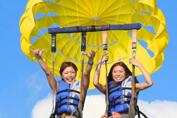 Two people parasailing with a yellow parachute against a blue sky.