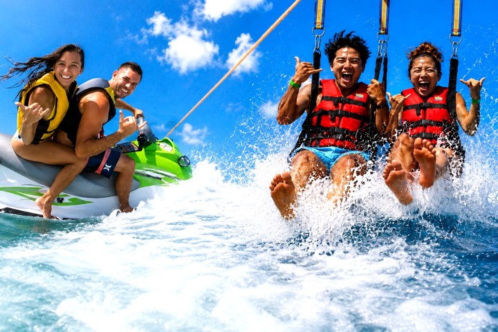 Four people having fun parasailing and jet skiing over clear blue ocean water.